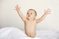 Portrait of funny nice baby girl stretching hands sitting in bed at home.