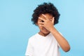 Portrait of funny nosy adorable little boy with curly hair covering face with hand and looking through fingers Royalty Free Stock Photo