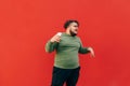 Portrait of a funny overweight young man standing on a red background with a smartphone in his hand, dancing and listening to