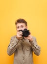 Portrait of funny photographer in shirt and glasses takes photo on camera against yellow background and looks into camera with Royalty Free Stock Photo