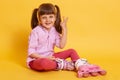 Portrait of funny pleasant little kid making gesture, raising two fingers, smiling sincerely, having rest, sitting on floor,