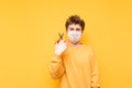 Portrait of a funny shaggy young man with scissors in his hands and a medical mask on his face stands on a yellow background and