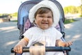 Portrait of funny smiling baby girl in white hat sitting in stroller, make faces Royalty Free Stock Photo