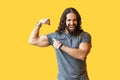 Portrait of funny strong bearded bodybuilder man with long curly hair in grey tshirt standing, pointing at his biceps and looking