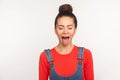 Portrait of funny stylish pretty girl with hair bun in denim overalls demonstrating tongue out expressing disobedience