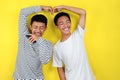 Portrait of funny young Asian men doing crazy lovely gesture, isolated on yellow