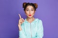 Portrait of funny young girl with two buns pointing finger upward like have idea, isolated over violet background in studio