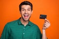 Portrait of funny young guy hold plastic card payment with no commission shopaholic advertisement nfc isolated on orange