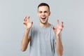 Portrait of funny young man in casual clothes shouting, growling like animal, making cat claws gesture isolated on grey Royalty Free Stock Photo