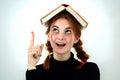 Portrait of funny young smiling student girl with an open book on her head holding her point finger up having an idea. Reading and Royalty Free Stock Photo