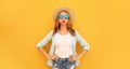 Portrait of funny young woman puffs out her cheeks with curly hair and straw hat on yellow background Royalty Free Stock Photo