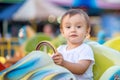 Portrait of future racing champion: toddler child sitting on little bright car on merry-go-round in theme park with proud face Royalty Free Stock Photo