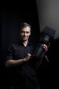 Portrait of a gaffer man with a professional lighting head device in his hands on a black background