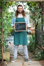 Portrait of gardener holding open text chalkboard at garden