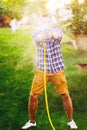 Portrait of gardener playing and smiling with water hose, watering the lawn, grass and plants