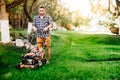 Portrait of young gardener using lawn mower for grass cutting in garden Royalty Free Stock Photo