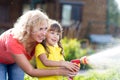 Portrait of gardener woman with daughter watering flowers on the lawn near cottage.