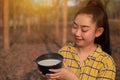 Portrait gardener young asea woman look at a full cup of raw para rubber milk of tree in plantation rubber tapping form Thailand,