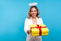 Portrait of generous angelic woman with halo on her wavy hair giving wrapped present box. isolated on blue background
