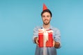 Portrait of generous kind cheerful man with party cone hat giving gift, congratulating on birthday and offering surprise