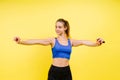 Portrait of gentle muscular woman holding skipping rope on her neck isolated over yellow background Royalty Free Stock Photo