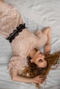 Portrait of a gentle sensual woman lying on white bed in a beige dress