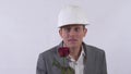 Portrait of genuine shy man in helmet extends a hand forward holding red rose. Shooting in the studio on a white