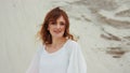 Portrait ginger woman in white dress, looking at camera, stone nature background.