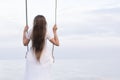 Portrait of girl. Back view. Young woman in white dress with loose hair sits on rope swing on sea backdrop Royalty Free Stock Photo