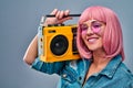 Portrait of girl with beaming smile in eyewear holding boom box on shoulder looking at camera  on grey background Royalty Free Stock Photo