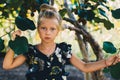 Portrait of a girl with blond hair in the garden in the summer under the crowns of trees