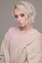 Portrait of girl of blonde with dark eye makeup and short hair in a pale pink sweater and beige oversized jacket, looking at camer