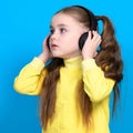 Portrait of a girl on a blue background in a yellow sweater, a little girl with wireless headphones.