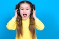 Portrait of a girl on a blue background in a yellow sweater, a little girl with wireless headphones.