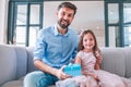 Portrait of girl and dad with gift box sitting on the sofa and looking at the camera Royalty Free Stock Photo