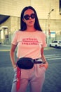 Portrait of a girl in dark sunglasses posing near a city mall. Dressed in white t-shirt, blue trousers, black waist bag Royalty Free Stock Photo