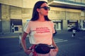 Portrait of a girl in dark sunglasses posing near a city mall. Dressed in white t-shirt, blue trousers, black waist bag Royalty Free Stock Photo