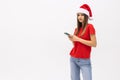 Portrait of a girl dressed in red christmas hat holding mobile phone while standing and looking at camera isolated over white Royalty Free Stock Photo