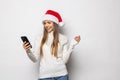 Portrait of a girl dressed in red christmas hat holding mobile phone while standing and looking at camera isolated over white Royalty Free Stock Photo