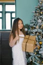 Portrait of girl in front of christmas tree holding gift looking at camera smiling Royalty Free Stock Photo