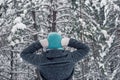 A girl in a gray coat and a light blue knitted hat stands in a beautiful winter snowy forest on a cloudy snowy day. Royalty Free Stock Photo