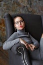 Portrait of a girl in a gray knit dress and glasses, sitting in a chair