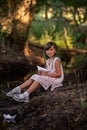 Portrait of girl with green hair sits on the river bank, holding white origami paper boat in hands