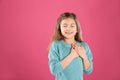 Portrait of girl holding hands near her heart on color background