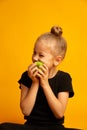 Portrait of girl kid bits apple. Pretty girl bits fresh apple on a yellow background
