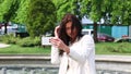 Portrait of girl laughing using smartphone. Pretty young woman with her mobile phone on fountain background. Pretty happy woman us