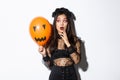 Portrait of girl looking scared at orange balloon with creepy face, wearing witch costume, celebrating halloween