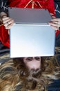 Portrait of a girl with loose blond hair. She is lying on a black bedspread, her laptop half-covering her face Royalty Free Stock Photo