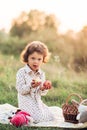 Portrait of a girl on a meadow in the sunset sunlight. Little girl in a light overalls sits on a blanket next to basket with harve