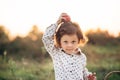 Portrait of a girl on a meadow in the sunset sunlight. Little girl in a light overalls sits on a blanket next to basket with harve